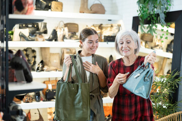 Elderly woman with young girl friend inspects shop window and is looking for modern, fashionable and roomy shoulder bag. In leather goods store, customers make choice of product with reasonable price