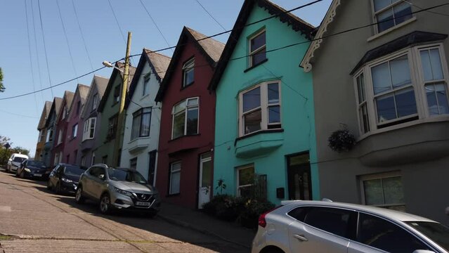 Cobh, Ireland, August 26, 2023: PAN SHOT - The St. Coleman&rsquo;s Cathedral and the Deck of Cards, a gravity-defying row of candy-colored houses stacked on a vertiginous hill, in Cobh, County Cork.