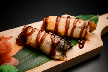 Fish rolls with brown sauce on a long green leaf on a black background