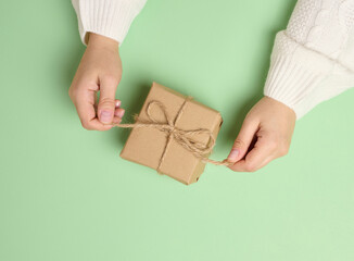Female hands holding a gift box on a green background. View from above