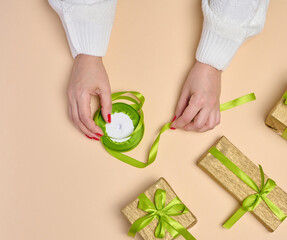 Female hands packing gifts on a beige background, top view