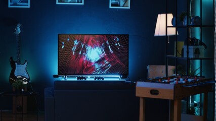 Panning shot of empty home studio illuminated with neon lights used for internet video production. Living room filled with content creation equipment, TV animations running in background - Powered by Adobe