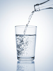 Water pouring from a bottle in a glass with bubbles on blue background