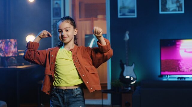Close up shot of energetic joyful kid doing charming dance moves for social media platform, following viral challenge. Joyous child recording video for online followers in dimly lit house