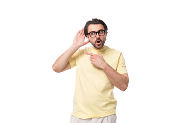 Fototapeta premium young handsome european brunette guy with a beard and mustache in glasses stands in surprise on a white background with copy space