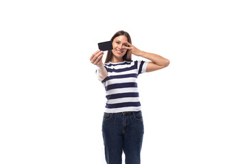 Fototapeta premium young brunette caucasian woman with light makeup dressed in a striped t-shirt and jeans holds out a plastic credit card with a mockup