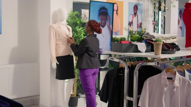 Meticulous worker closing buttons on mannequin blazer after restocking elegant high end fashion boutique. Woman tidying up stylish garments from new collection after changing old season clothing