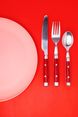 Empty plate, Spoon, fork, knife, on a red background, top view. Space for text.