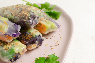 Vegetarian vietnamese spring rolls with carrot, cucumber, red cabbage, cilantro, sesame and rice noodle on a pink plate. veggie dish. Vegan food. Horizontal orientation. Selective focus. Copy space