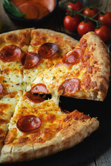 A slice of hot Italian pizza with stretching cheese. Pizza pepperoni on a dark wooden background