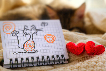 Fun picture on paper, notepad and two red hearts. Pretty cute kitten relaxing on the bed. Tabby...