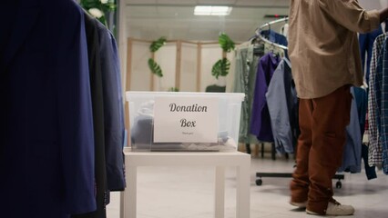 Customers donating stylish formal clothes in thrift shop, doing good deed. Generous clients adding their garments in donation box for charitable event organized by SH clothing store