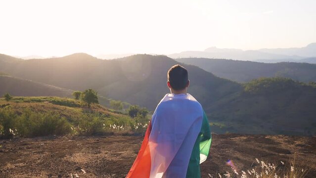 Man with the Italian flag wrapped around him atop a mountain with the sunset in the mountains. Wrapped in patriotism, exemplifying the spirit of 'Forza Italia!' during moments of national pride.