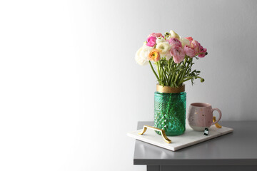 Bouquet of beautiful ranunculuses and tea on table near light grey wall. Space for text