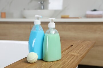 Wooden tray with bottles of shower gels and bath bomb on tub indoors, space for text