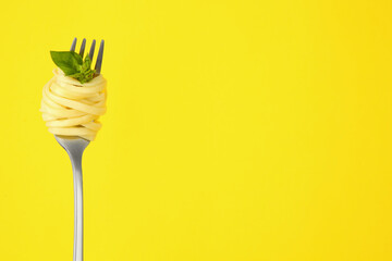 Fork with tasty pasta and basil on yellow background, space for text