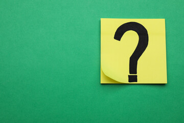 Sticky note with question mark on green background, top view. Space for text