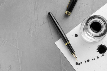 Stylish fountain pen, paper with drops of ink and inkwell on grey textured table, flat lay. Space...