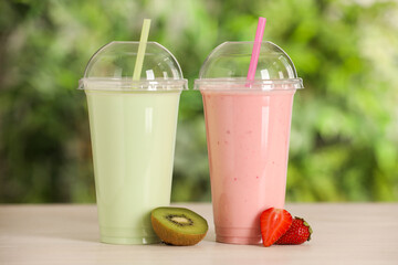 Plastic cups with different tasty smoothies and fresh fruits on wooden table outdoors