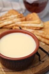 Tasty condensed milk and crepes on wooden board, closeup