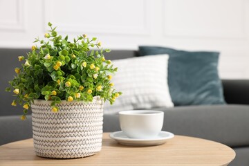 Potted artificial plant and cup of drink on coffee table near sofa indoors, closeup