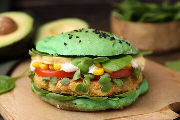 Tasty green vegan burger with vegetables, patty and microgreens on wooden board, closeup