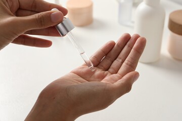 Woman applying cosmetic serum onto her hand at white table, closeup