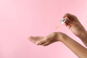 Woman applying cosmetic serum onto her hand on pink background, closeup. Space for text