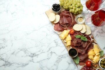 Charcuterie board. Delicious bresaola, wine and other products on white marble table, flat lay....