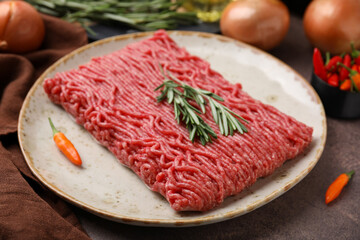 Fresh raw ground meat, chili peppers and rosemary on brown table, closeup