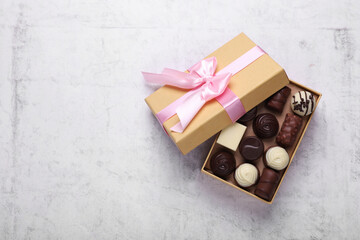 Open box with delicious chocolate candies on white table, top view. Space for text