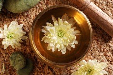 Tibetan singing bowl with water, beautiful chrysanthemum flowers, mallet and stones on table, flat lay