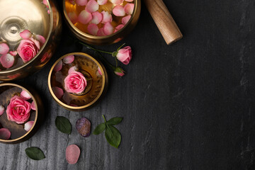 Tibetan singing bowls with water, beautiful rose flowers and mallet on gray table, flat lay. Space...