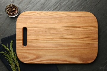Wooden cutting board and spices on dark grey table, flat lay