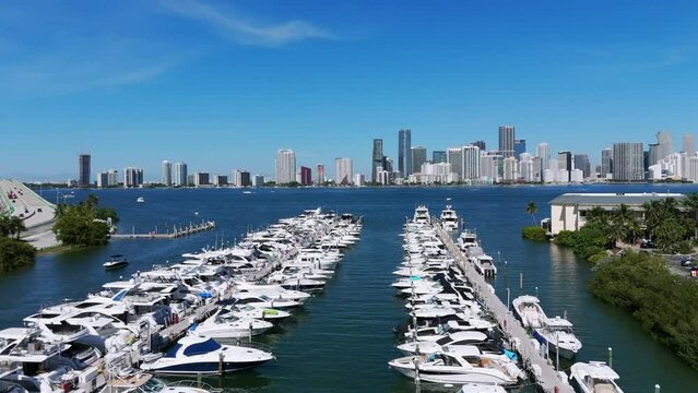 Rows of upper-class yachts at anchor park and modern american megapolis on background. Private boats in lovely Rickenbacker Marina next to roadbridge and Miami Marine Stadium