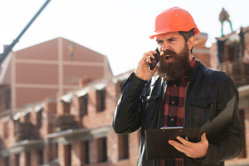 Construction worker on construction site, building business. Portrait of man builder in hardhat working at construction site, talking on phone.