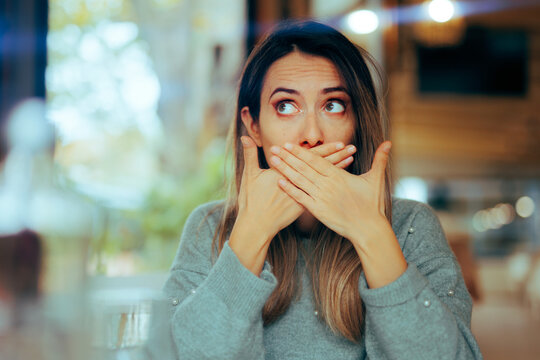 Burping Woman Covering her Mouth in a Restaurant. Sick girl feeling nauseated and gassy after her meal 
