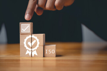 A hand holding wooden cubes with ISO icons symbolizes the concept of quality control and assurance....