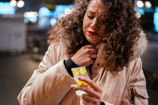 Young woman in the city streets in winter having sore throat and using lozenges 