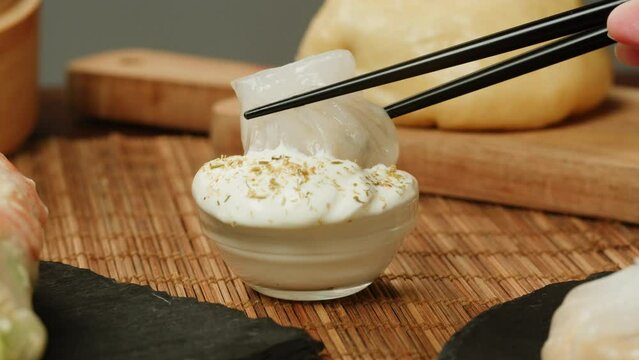 Dipping dimsun into white sauce close-up macro. Dim sun, gedza dumplings, spring rolls on the table. Food delivery