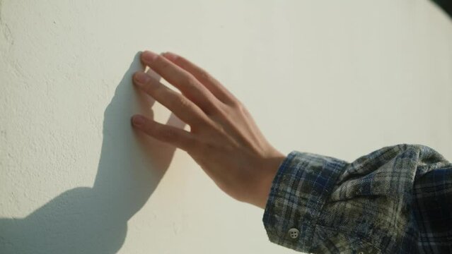 Woman hand is touching a white concrete surface close up macro. Female is stroking stone rock wall. 