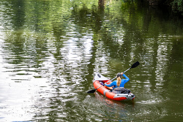 Woman on an inflatable kayak boat with an oar in her hands paddles on the lake preferring an active lifestyle