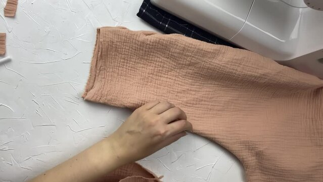 Seamstress cut off extra thread on a cotton muslin fabric with scissors. Workshop of a fashion designer. Needlewoman checks the seams and the appearance of the new clothes. Craft and hobby.