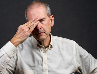 A man in his 60s holds the side of his head in discomfort. Migraine Pain management concept.