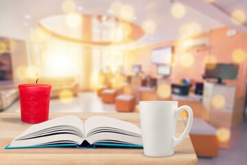 Coffee cup and burning candle on table in bedroom.