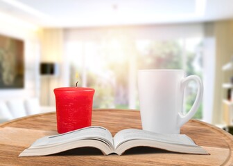 Coffee cup and burning candle on table in bedroom.