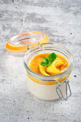 Mango panna cotta dessert with mango slices and mint in a glass mug on a gray concrete background