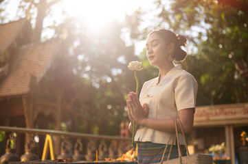 A beautiful Asian woman in a traditional Thai-Lanna dress is making a wish in a temple.