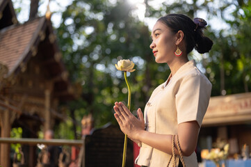 A beautiful Asian woman in a traditional Thai-Lanna dress is making a wish in a temple. Thai culture