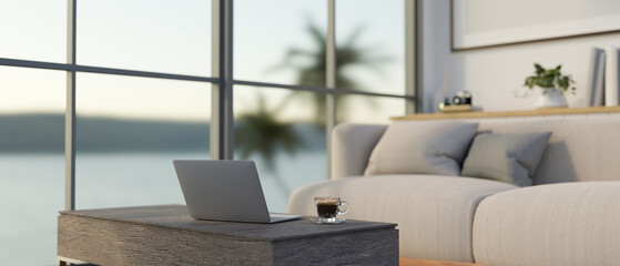 A laptop on a coffee table in a modern apartment living room with a cosy couch near by the window.